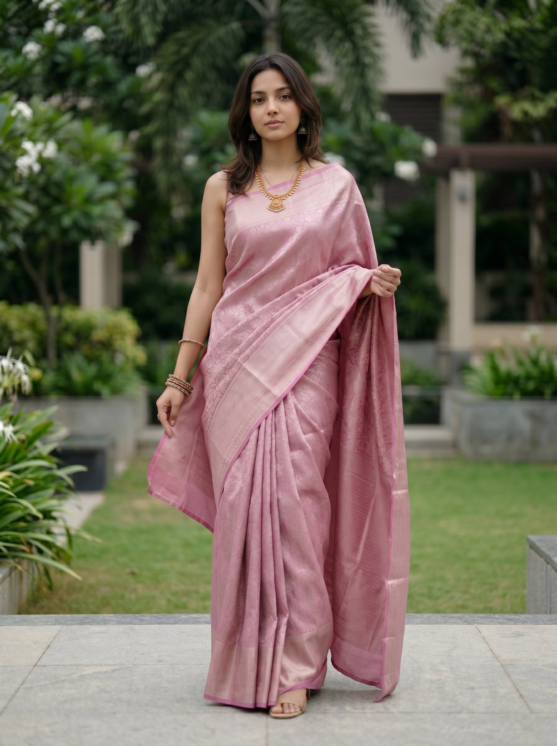 Woman in a pink saree standing outdoors with greenery in the background