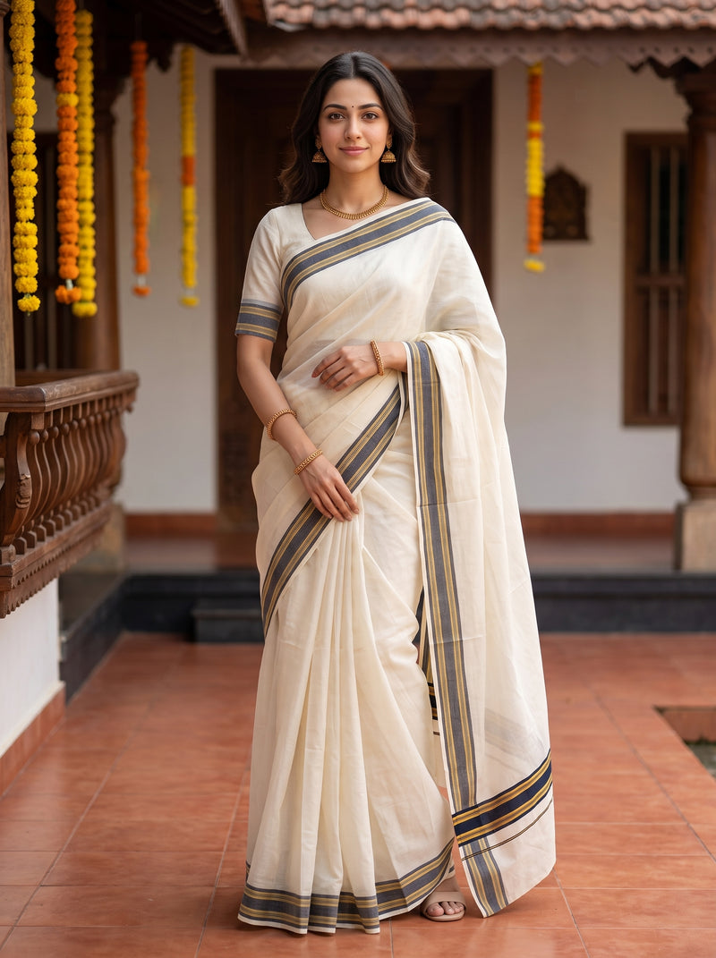 A woman wearing a cream-colored cotton saree with blue and gold striped borders, standing in a traditional courtyard with terracotta tiled floors and hanging yellow marigold garlands.