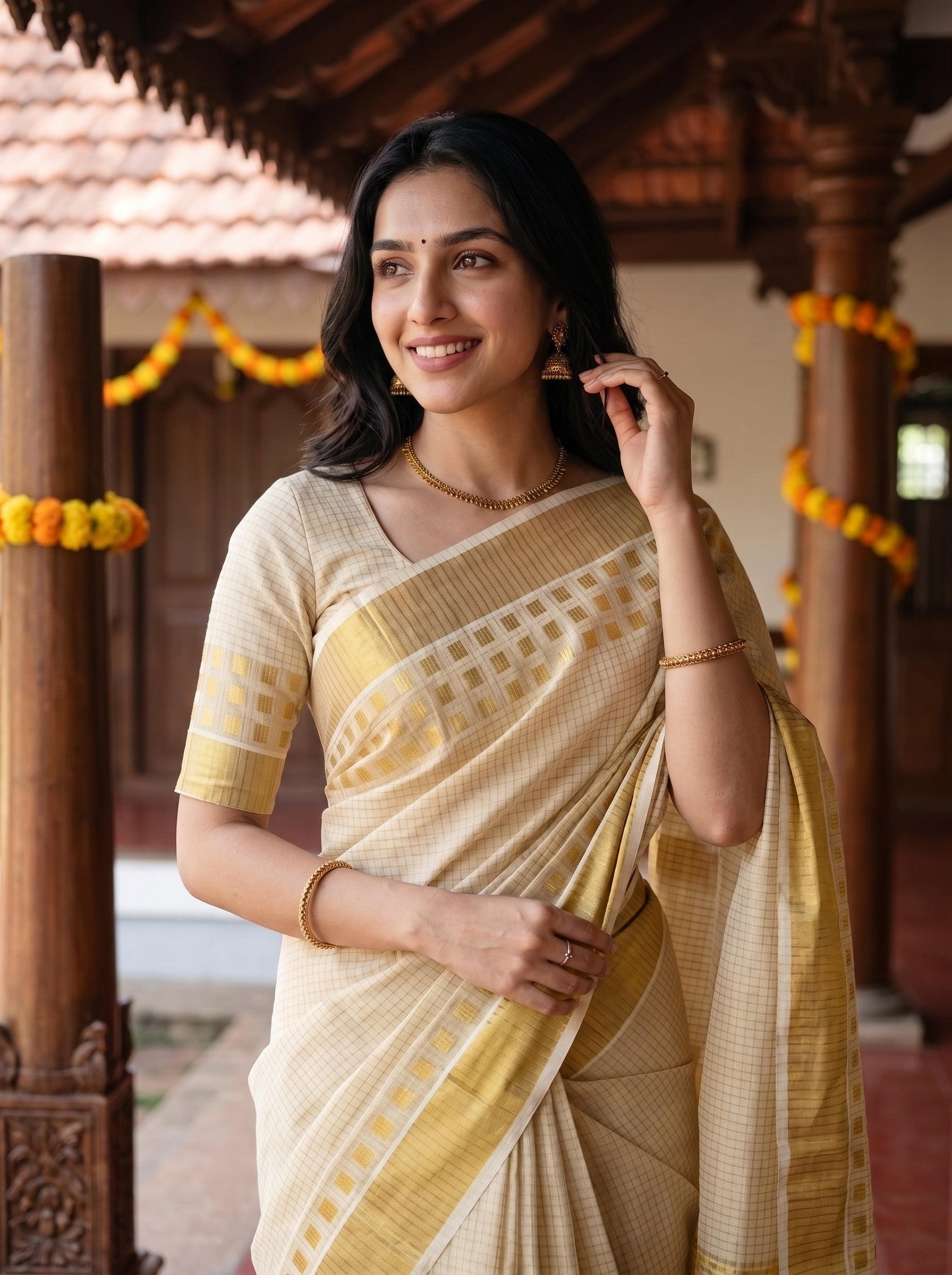A woman wearing a traditional Indian saree in beige and yellow-gold, standing in a courtyard with wooden pillars and yellow garlands.