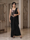 Woman in a black saree with a decorative blouse standing indoors.