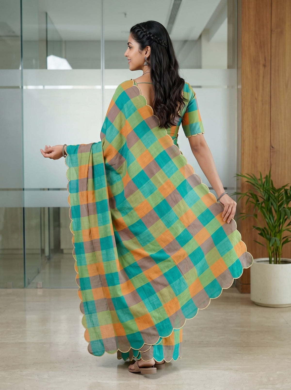 A woman wearing a colorful checkered saree with a matching blouse, photographed from behind in a modern glass-walled indoor space.