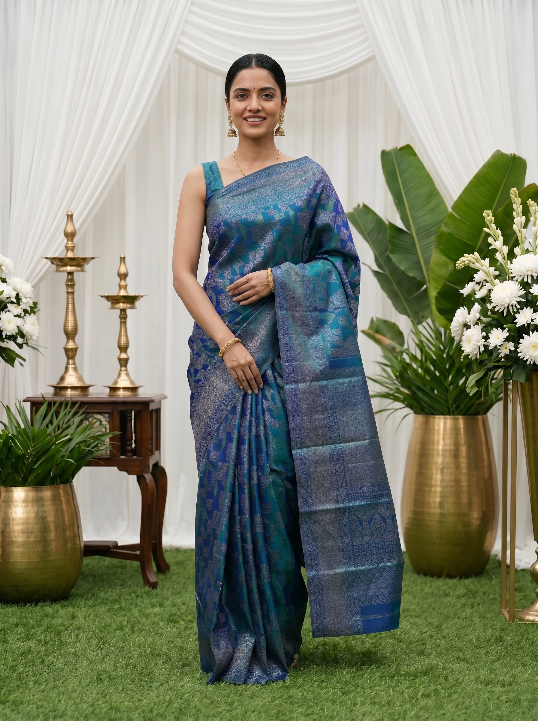 Woman in a blue saree standing in a decorated indoor setting with plants and floral arrangements.
