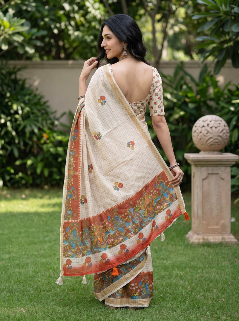 A woman wearing a cream-colored saree with a colorful floral border and matching printed blouse, standing in a garden setting.