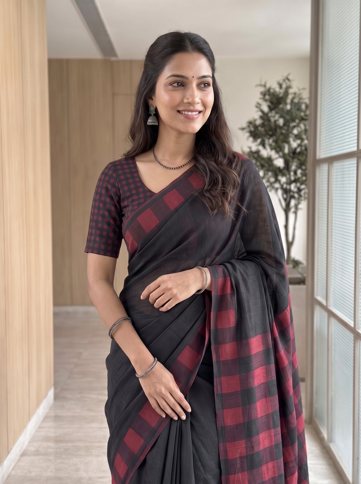 A woman modeling a black and red buffalo check plaid saree with a matching checkered short-sleeve blouse, standing in a modern indoor hallway.