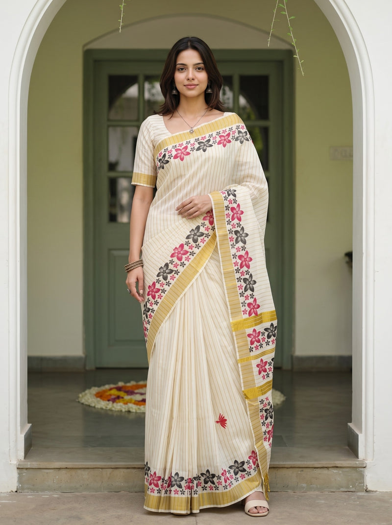 A woman models a cream-colored saree with pink, green, and gold floral embroidery, standing in a doorway.