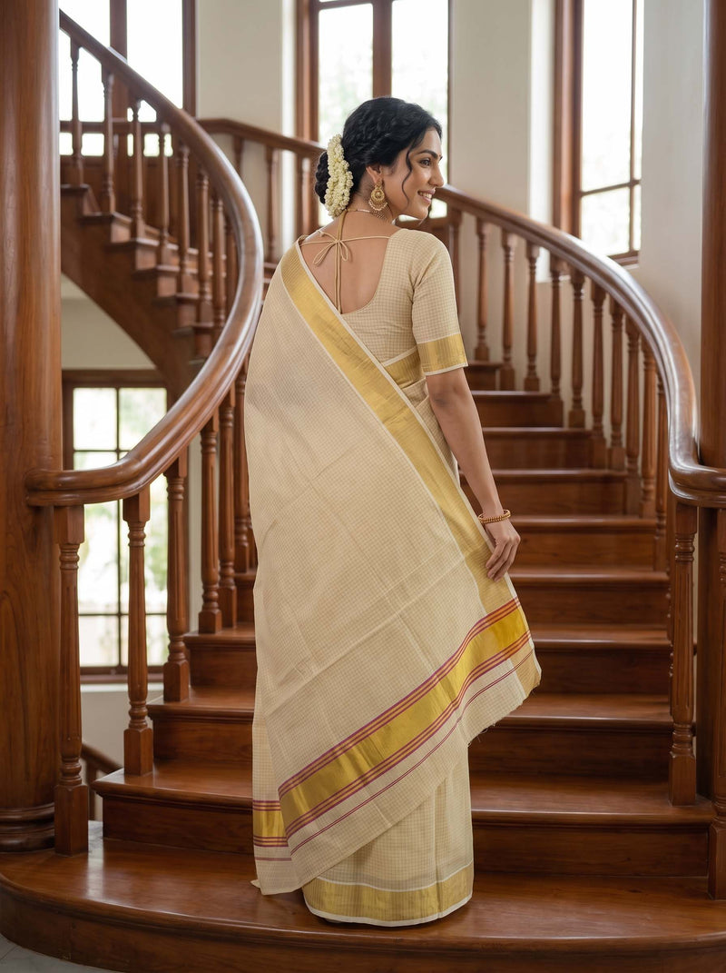 A woman wearing a cream-colored saree with yellow and red border stripes, standing on a wooden staircase in a home interior.