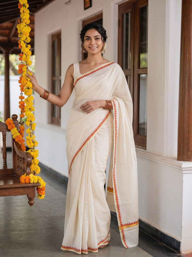 A woman wearing a cream-colored cotton saree with orange and yellow border details, standing in a traditional house corridor decorated with yellow marigold garlands.
