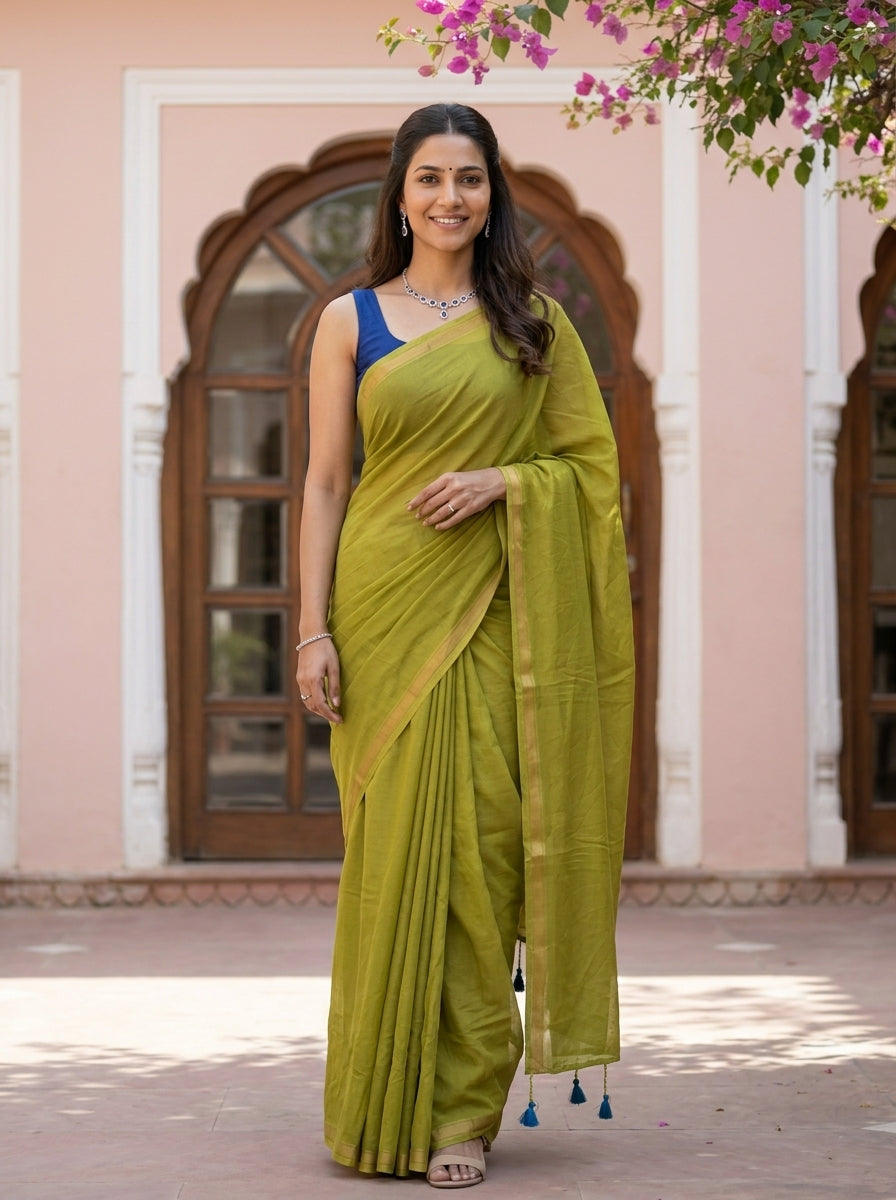 Woman in a green saree with a blue blouse standing in front of a pink building.