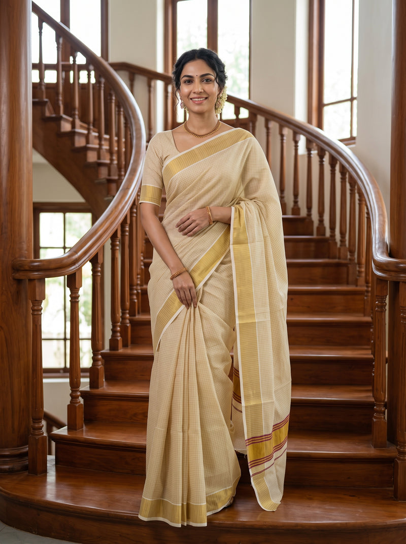 A woman wearing a cream-colored silk saree with yellow and red stripes, standing on a wooden staircase in a home interior.