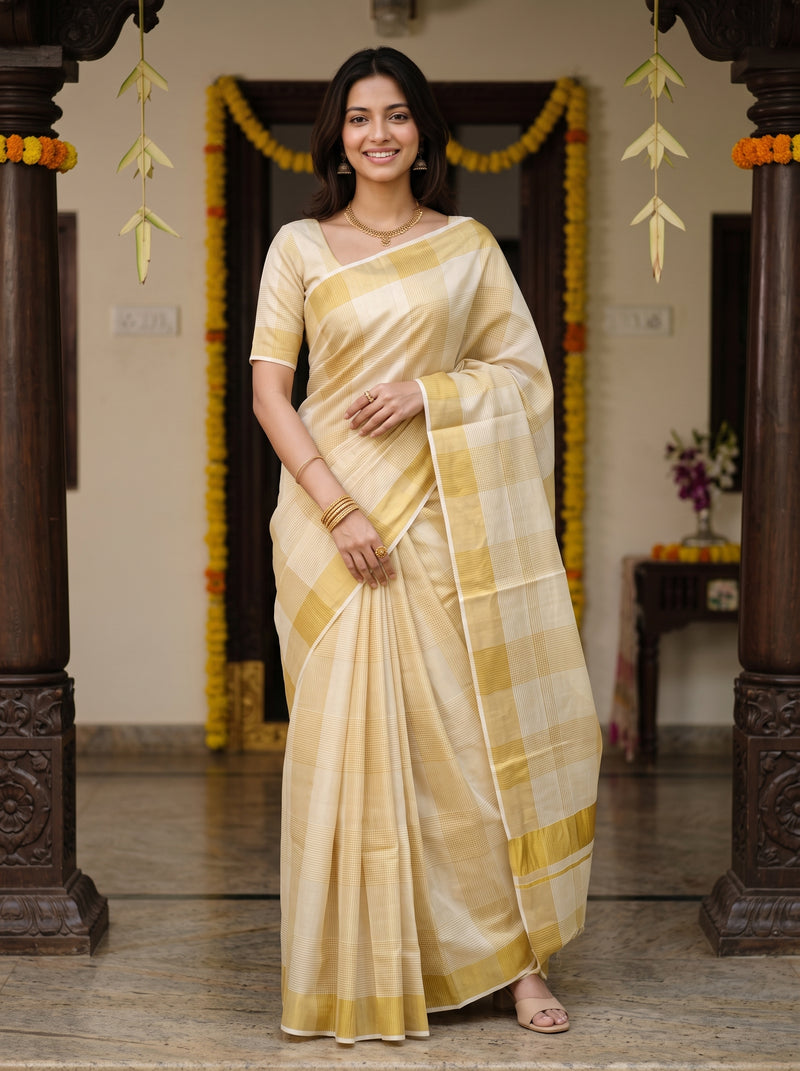 A woman wearing a light beige and yellow checkered silk saree with a matching short-sleeve blouse, standing in a decorated traditional indoor setting.