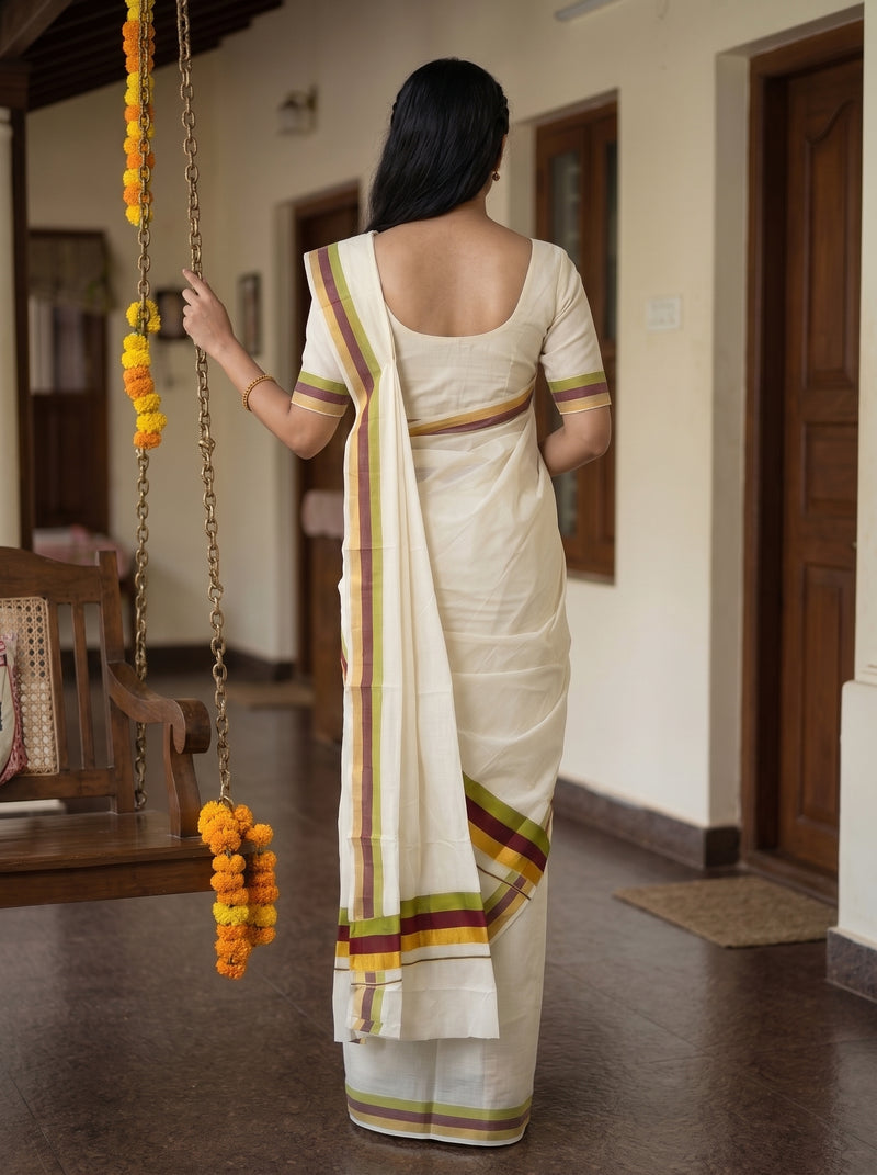A woman viewed from behind wearing a cream-colored cotton saree with a matching short-sleeve blouse. The saree features thin stripes of green, yellow, and red along the border and pallu.
