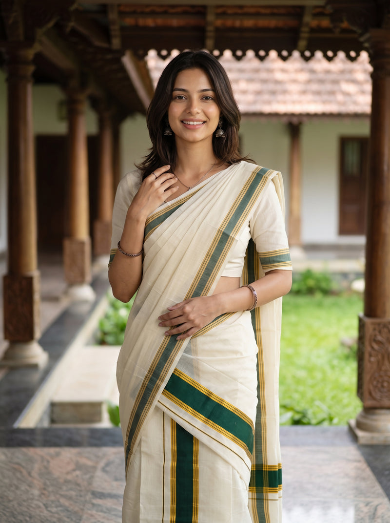 A woman wearing a cream-colored sari with green and gold stripes, standing in a traditional courtyard with wooden pillars and greenery in the background.
