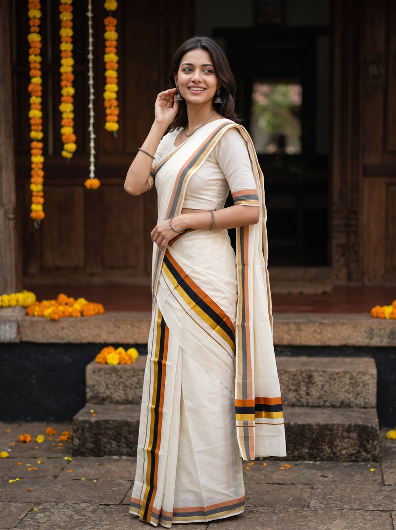 A woman wearing a cream-colored cotton saree with orange, yellow, and black stripes, standing in front of a traditional wooden doorway decorated with marigold garlands.