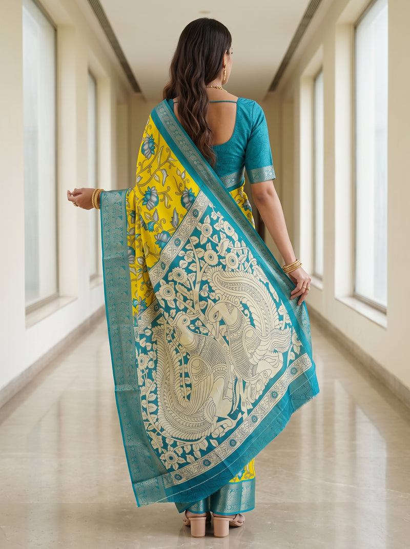 A woman viewed from behind wearing a bright yellow and teal blue saree with intricate white and gold zari embroidery, standing in a brightly lit hallway.