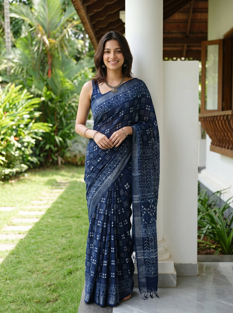 Woman wearing a blue saree standing outdoors with greenery in the background
