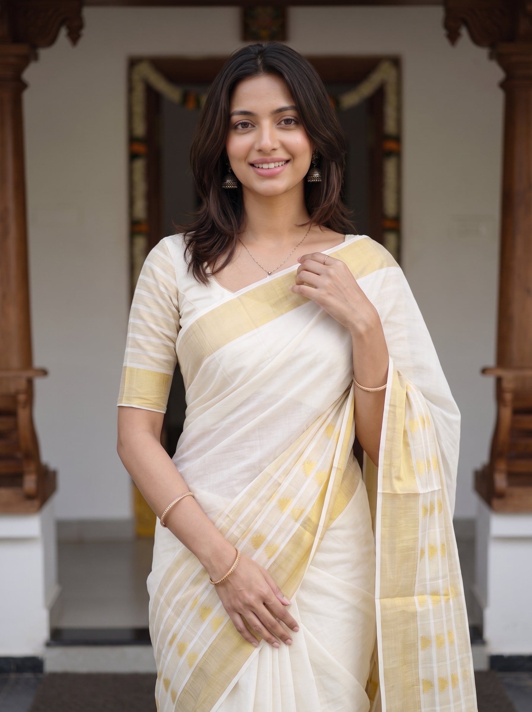 A woman wearing a cream and pale yellow silk saree with a matching blouse, standing in front of a traditional architectural background.