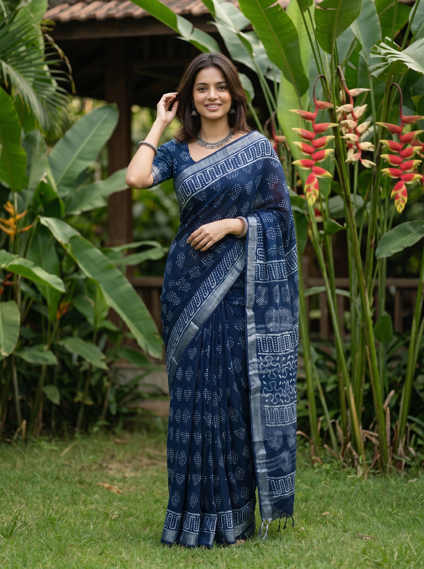 Woman in a blue saree standing in a garden with greenery and flowers.