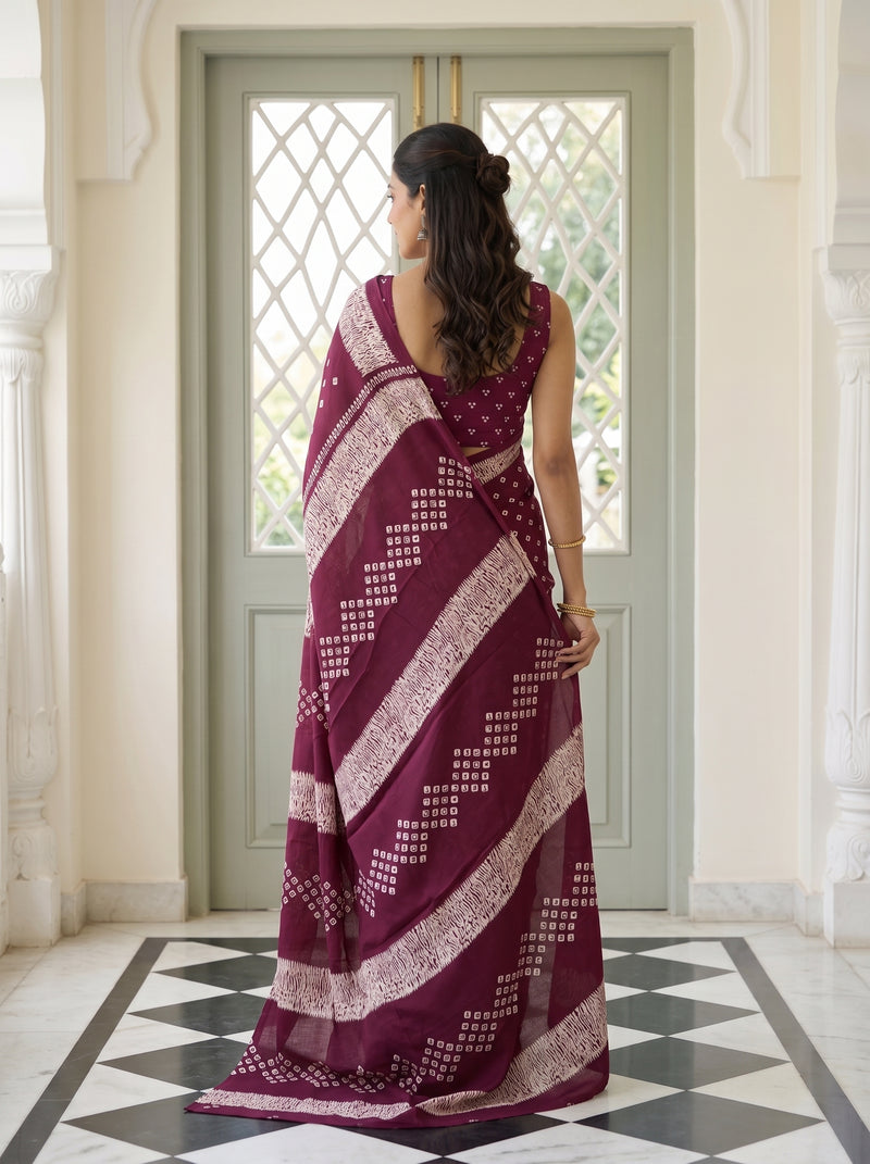 A woman stands with her back to the camera wearing a deep maroon saree with white block prints and a matching printed blouse, posed in front of a light green door in an elegant interior.