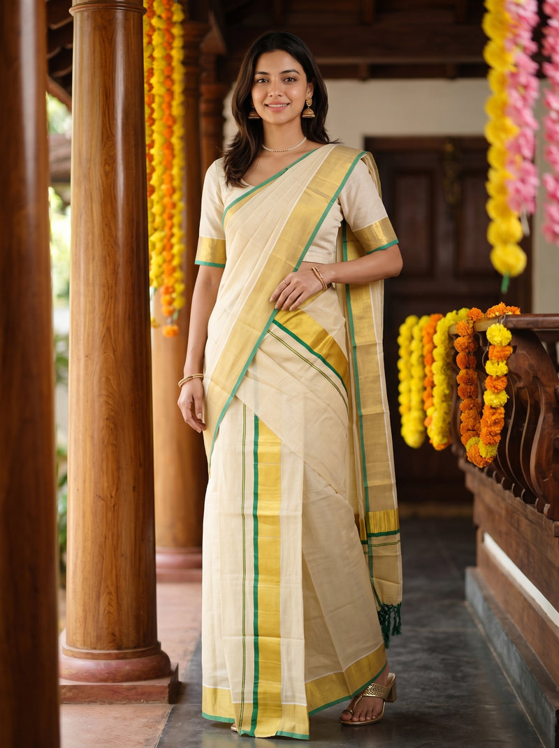 A woman modeling a cream-colored cotton saree with yellow and green borders, standing in a traditional corridor decorated with yellow and orange marigold garlands.