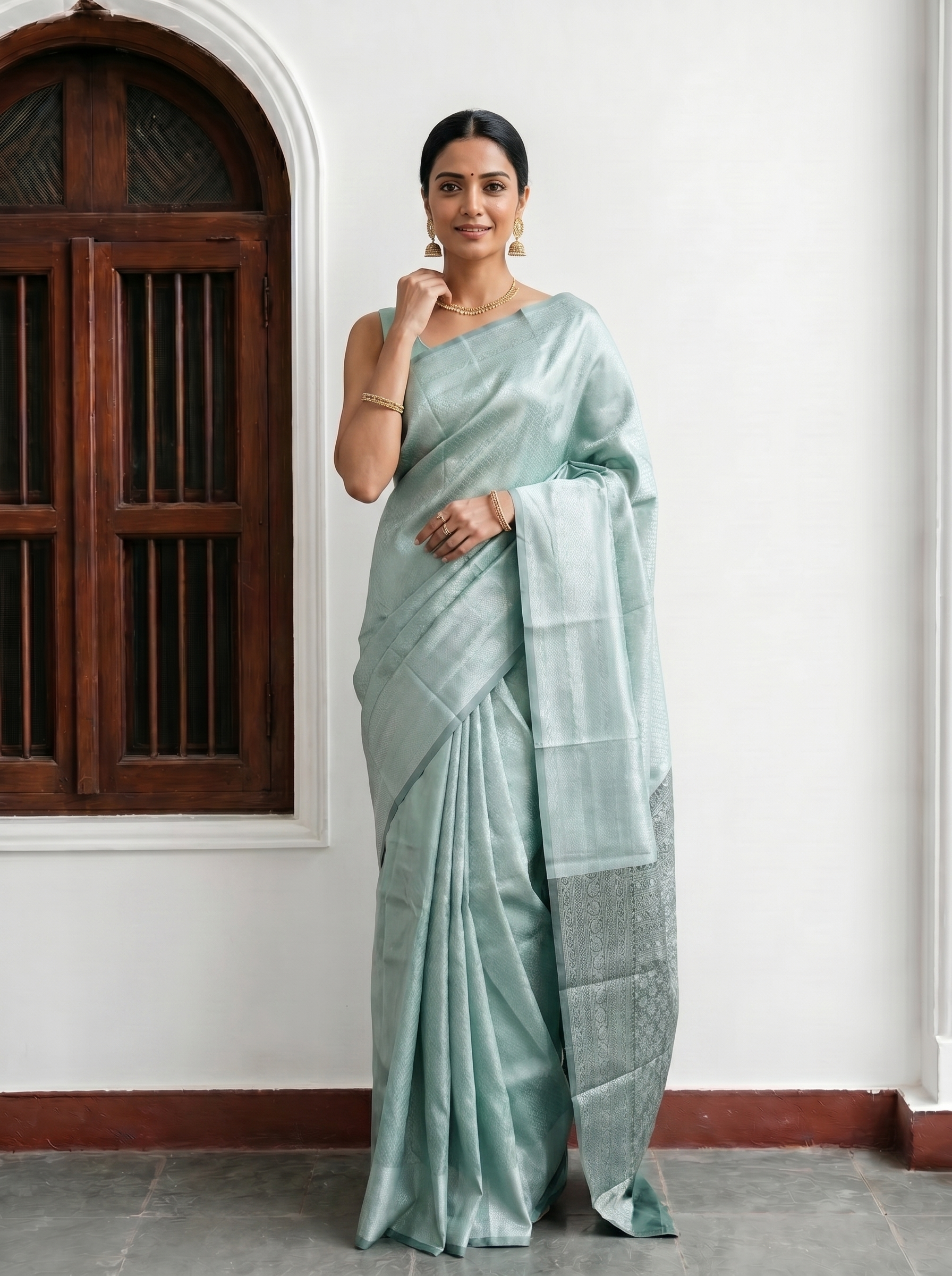 Woman wearing a light green saree in an indoor setting with a wooden door and white wall.